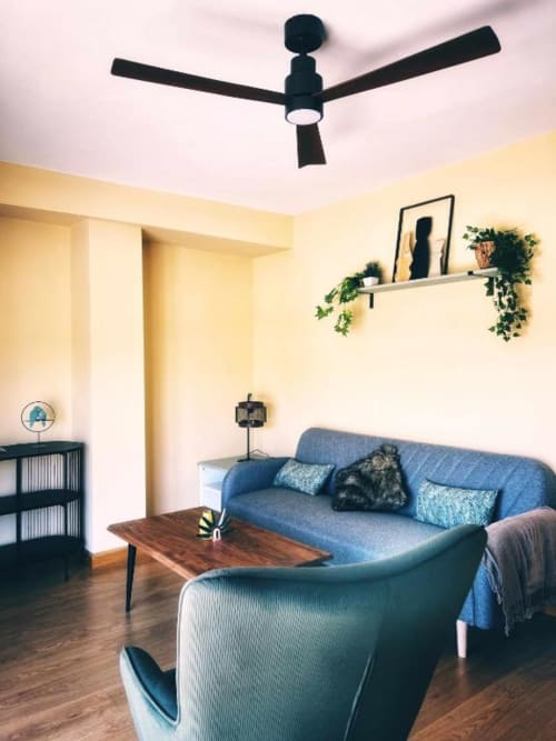 Moderno salón de apartamento en AlmaMaterSalamanca con sofá azul, ventilador de techo, paredes amarillas y pisos de madera
