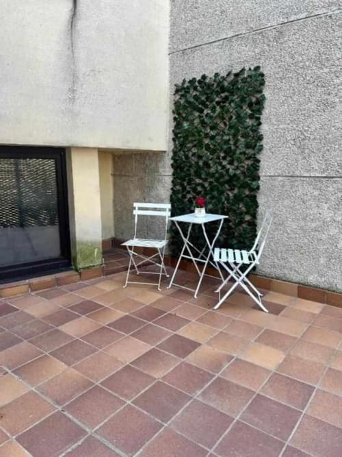 Acogedor patio de Apartamentos AlmaMaterSalamanca con muebles blancos, baldosas de barro y muro cubierto de hiedra verde