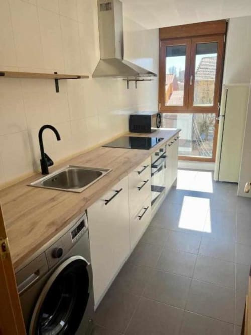 Cocina moderna en apartamento de Salamanca con muebles blancos, encimeras de madera, electrodomésticos de acero inoxidable y luz natural