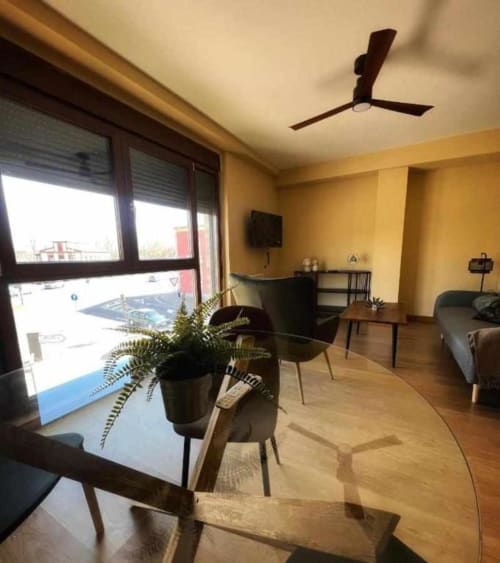 Moderna sala de estar en Salamanca con muebles de madera, plantas en macetas, ventilador de techo y vista al balcón de la ciudad