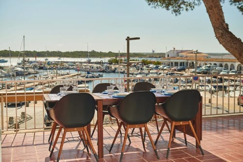 Waterfront dining terrace with modern chairs overlooking Colonia de Sant Jordi marina and sailboats