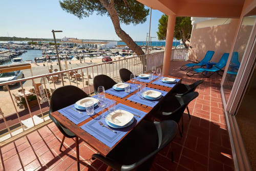 Waterfront dining terrace in Colonia de Sant Jordi with set table, marina views, and blue loungers