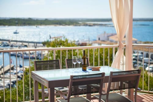 Waterfront balcony dining at Colonia de Sant Jordi with marina views, wine glasses, and shaded seating overlooking the