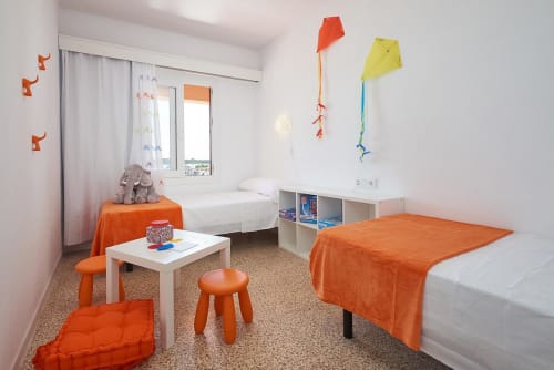 Colorful children's bedroom at Colonia de Sant Jordi hotel with orange accents, twin beds, and kites decorating white walls.