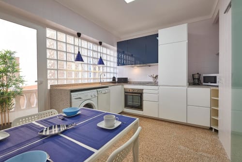 Modern kitchen with white cabinets, blue accents, and dining table at Enjoy the sea in Colonia de Sant Jordi