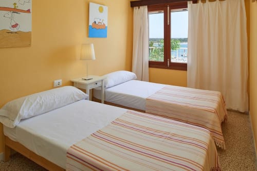 Twin bedroom with yellow walls, sea view windows, and striped bedcovers at Colonia de Sant Jordi hotel