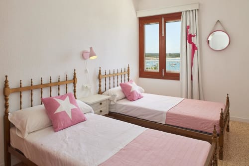 Twin bedroom with wooden beds, pink accents, and sea view at Colonia de Sant Jordi hotel
