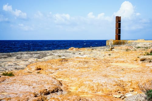 Paisaje costero rocoso con faro oxidado de color herrumbre dominando el azul mar en Colonia de Sant Jordi