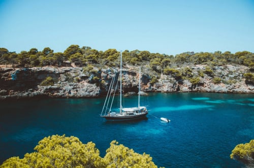 Sailboat anchored in crystal-clear turquoise waters near Colonia de Sant Jordi with rocky coastline