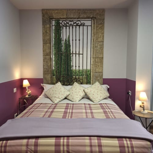 Elegant bedroom at Locanda del Sasso with burgundy accent wall, plaid bedding, and decorative metal gate headboard in Crodo,
