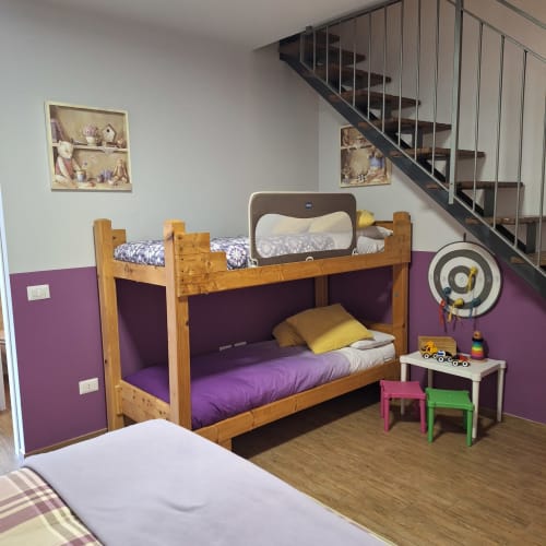 Child's bedroom at Locanda del Sasso with wooden bunk bed, purple walls, colorful stools, and staircase in Crodo.
