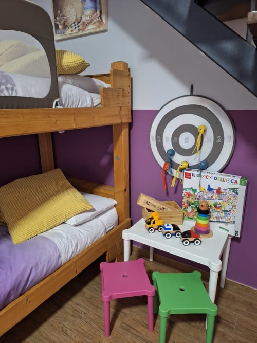 Colorful children's bedroom at Locanda del Sasso with wooden bunk beds, purple walls, toys, and numbered dartboard