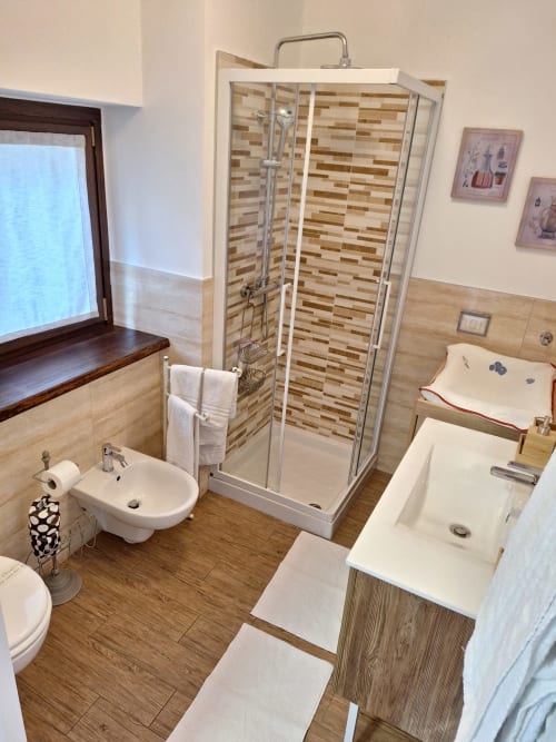 Modern bathroom at Locanda del Sasso Rooms in Crodo with shower enclosure, white sink, toilet, and wooden flooring