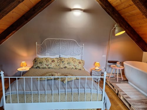Cozy attic bedroom at Locanda del Sasso in Crodo with ornate metal bed, floral bedding, wooden beams, and en-suite bathroom