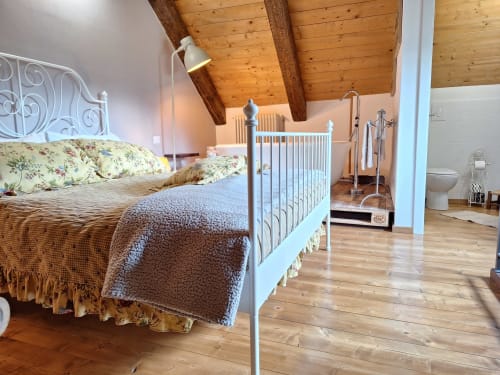 Rustic bedroom with wooden beams at Locanda del Sasso in Crodo, featuring white iron bed and ensuite bathroom