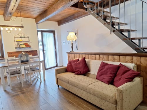 Modern loft apartment at Locanda del Sasso in Crodo with wooden beams, beige sofa, red pillows, and spiral staircase
