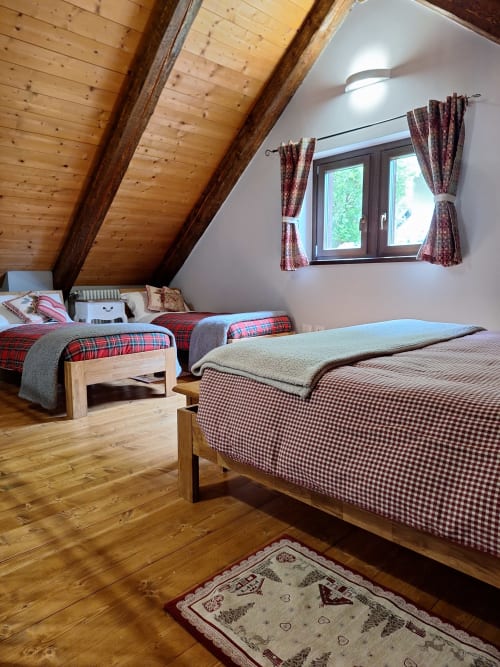Accogliente camera da letto in soffitta presso Locanda del Sasso a Crodo, con travi in legno, più letti, coperte scozzesi rosse e vista sulle montagne