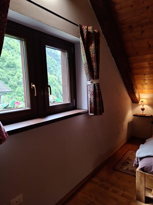 Accogliente camera da letto in Locanda del Sasso con vista montagna, finestre scure, travi in legno e illuminazione calda