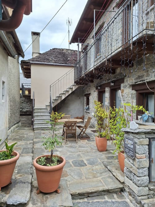 Charmanter Innenhof der Locanda del Sasso Rooms in Crodo mit Steinpatio, Topfpflanzen und Holzsitzbereich