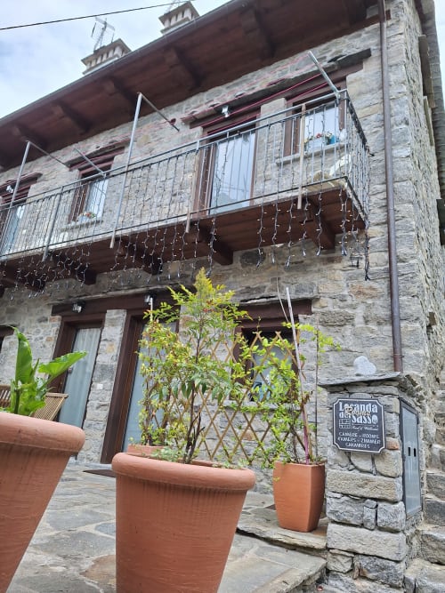 Steingebäude der Locanda del Sasso mit Balkon, Blumenkübeln und Windklängen in Crodo, Italien