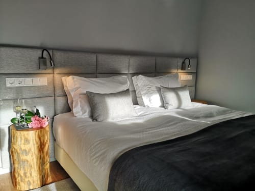 Quarto moderno em Em Xisto com cabeceira estofada cinza, roupa de cama branca, criado de madeira com flores cor-de-rosa e iluminação ambiente