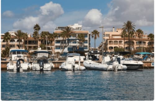 Marina con barcos blancos y yates atracados en el paseo marítimo de Colonia de Sant Jordi, localidad turística mediterránea con palmeras