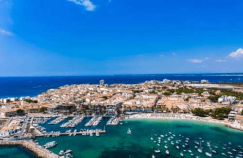 Vista aérea de la bahía turquesa de Colonia de Sant Jordi con puerto, embarcaciones y edificios frente al mar bajo cielo azul