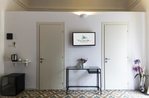 Modern hotel room entrance at C'era una Volta in Palermo, showing white doors, desk with purple flowers, and patterned tile