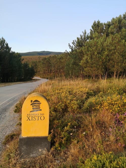 Marcador amarelo de Aldeias do Xisto em estrada rural com floresta de pinheiros e montanhas, Góis Portugal