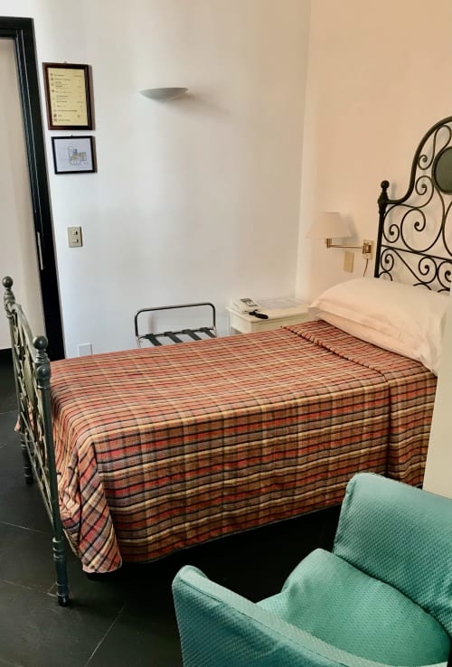 Einzelzimmer des Hotel Beau Rivage in Alassio mit roter Wolldecke, schmiedeeisernem Kopfteil und grünem Stuhl