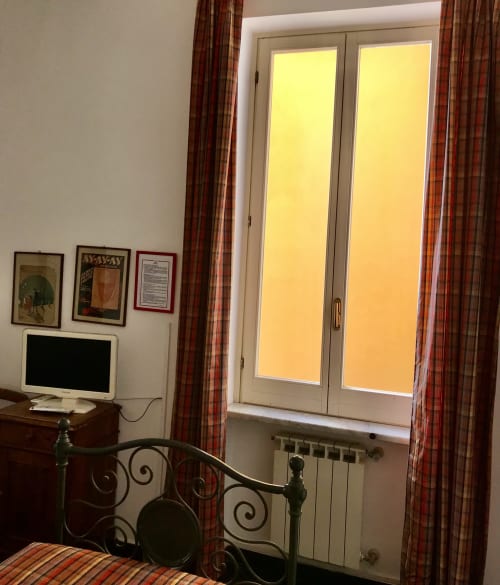 Einzelzimmer des Hotel Beau Rivage mit Bett, Fernseher, Schreibtisch und Glastüren mit Blick auf die Stadt Alassio mit roten karierten Vorhängen