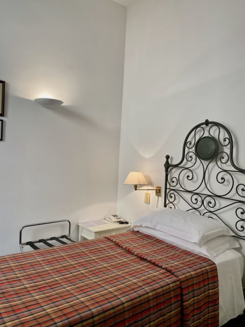 Gemütliches Einzelzimmer im Hotel Beau Rivage in Alassio mit Schmiedeeisenbett, rot gestreifter Decke und Wandleuchten