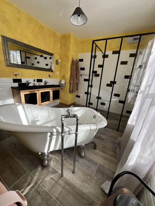 Salle de bain luxueuse aux murs jaunes, baignoire îlot et douche moderne à cadre noir au gîte Les papillons de baccara
