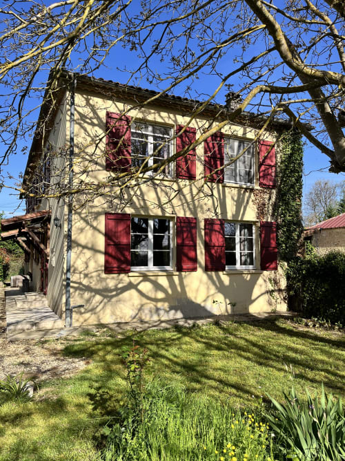 Charmant cottage crème aux volets bordeaux à Les papillons de baccara à Gondrin, France, entouré d'arbres nus