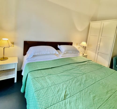 Helles Schlafzimmer im Hotel Beau Rivage in Alassio mit grüner gesteppter Tagesdecke, weißen Kissen und dunklem Holzkopfteil