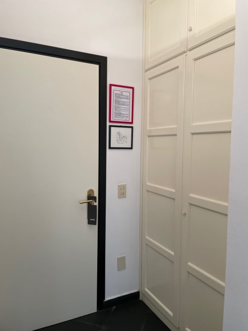 Flureingang mit schwarzgerahmter Tür, cremefarbenem Kleiderschrank und wandmontierten Dokumenten im Hotel Beau Rivage, Alassio