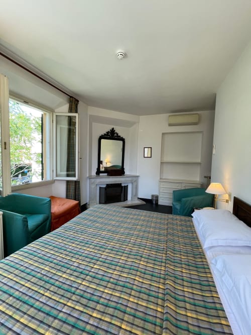 Chambre classique avec cheminée à l'Hôtel Beau Rivage d'Alassio, literie rayée, fauteuils verts et vue sur la ville