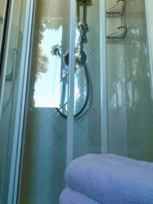 Dusche mit Meerblick im Hotel Beau Rivage, Strandfront-Zimmer mit Palmen sichtbar durch Glastüren