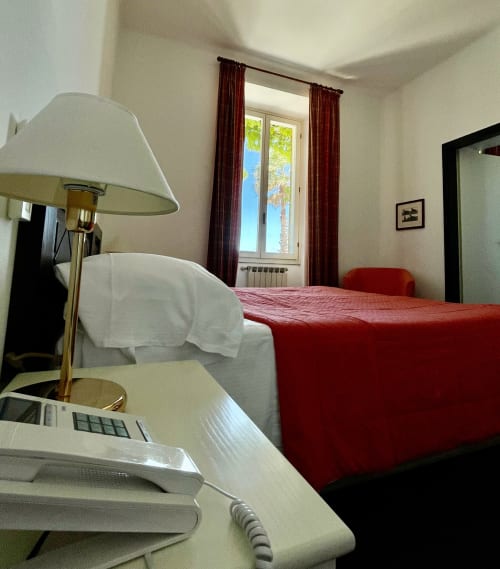 Meerblickzimmer des Hotel Beau Rivage in Alassio mit rotem Bett, Schreibtisch mit Lampe und Blick auf Palmen durch Glastüren