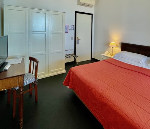 Geräumiges Schlafzimmer im Hotel Beau Rivage in Alassio mit roter Bettwäsche, dunklem Boden, weißem Kleiderschrank, Schreibtisch und Nachttischlampe