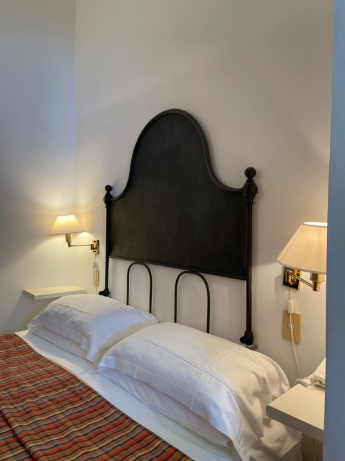 Elegantes Zimmer des Hotel Beau Rivage Alassio mit schwarzem Schmiedeeisen-Kopfteil, weißen Kissen und Messingwandleuchten