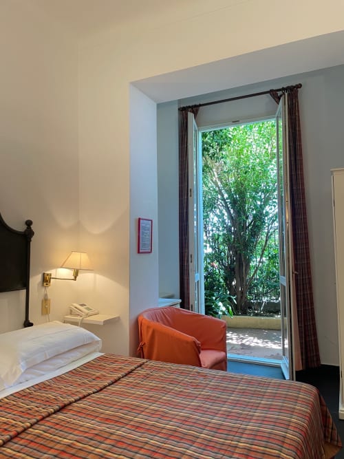 Zimmer des Hotel Beau Rivage in Alassio mit Gartenblick, gestreiftem Bettzeug, Nachttischlampe und Türen zur Terrasse