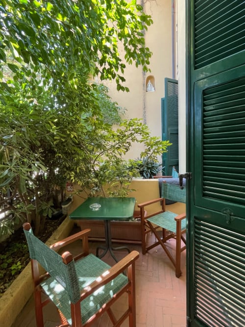 Gemütliche Terrasse des Hotel Beau Rivage in Alassio mit grünem Tisch, hölzernen Stühlen und üppigem Efeu, mit Blick auf eine cremefarbene Wand