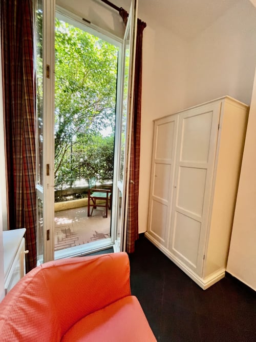 Helles Hotelzimmer mit rotem Sessel, offene Glastüren zur Gartenterrasse mit Grün im Hotel Beau Rivage, Alassio