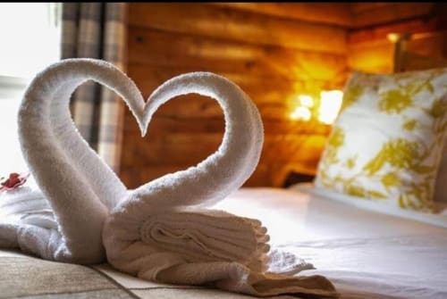 Two white towels folded into heart shapes on a bed at Grouse Lodge cottage in Dunoon, with warm interior lighting