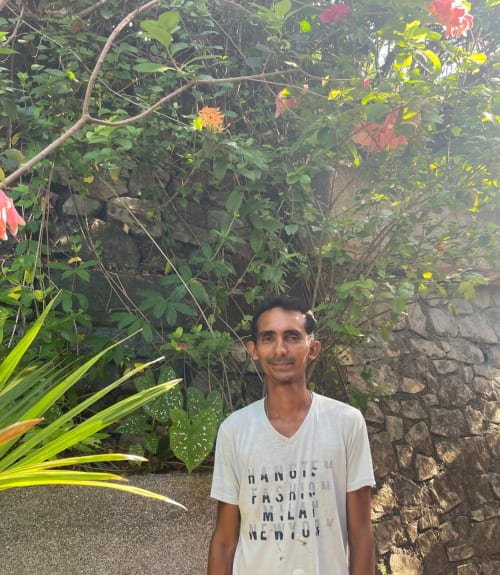 Man posing in lush garden at Villa Mango B&B, Nosara, Costa Rica with tropical flowers and stone wall