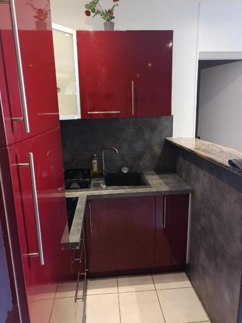 Cuisine moderne avec meubles rouges brillants, crédence noire et évier en acier inoxydable dans un appartement de Pont-Sainte-Maxence