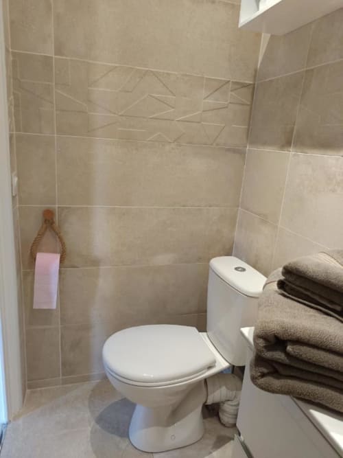 Salle de bain moderne aux murs en carrelage beige, toilettes blanches, lavabo et serviettes pliées à l'appartement Pont-Sainte-Maxence