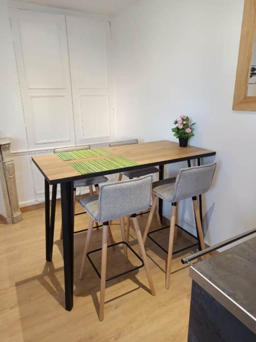 Bar de cuisine moderne avec table en bois, sets de table à rayures vertes et tabourets gris capitonnés dans un appartement lumineux.