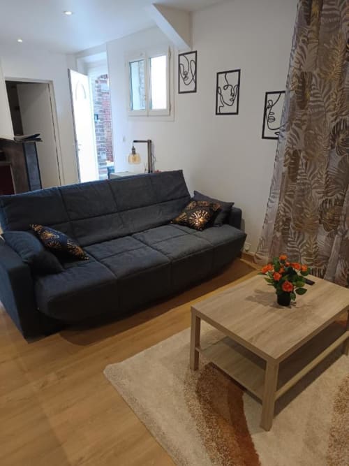 Salon moderne d'appartement avec canapé gris foncé, table en bois et fleurs orangées à Pont-Sainte-Maxence